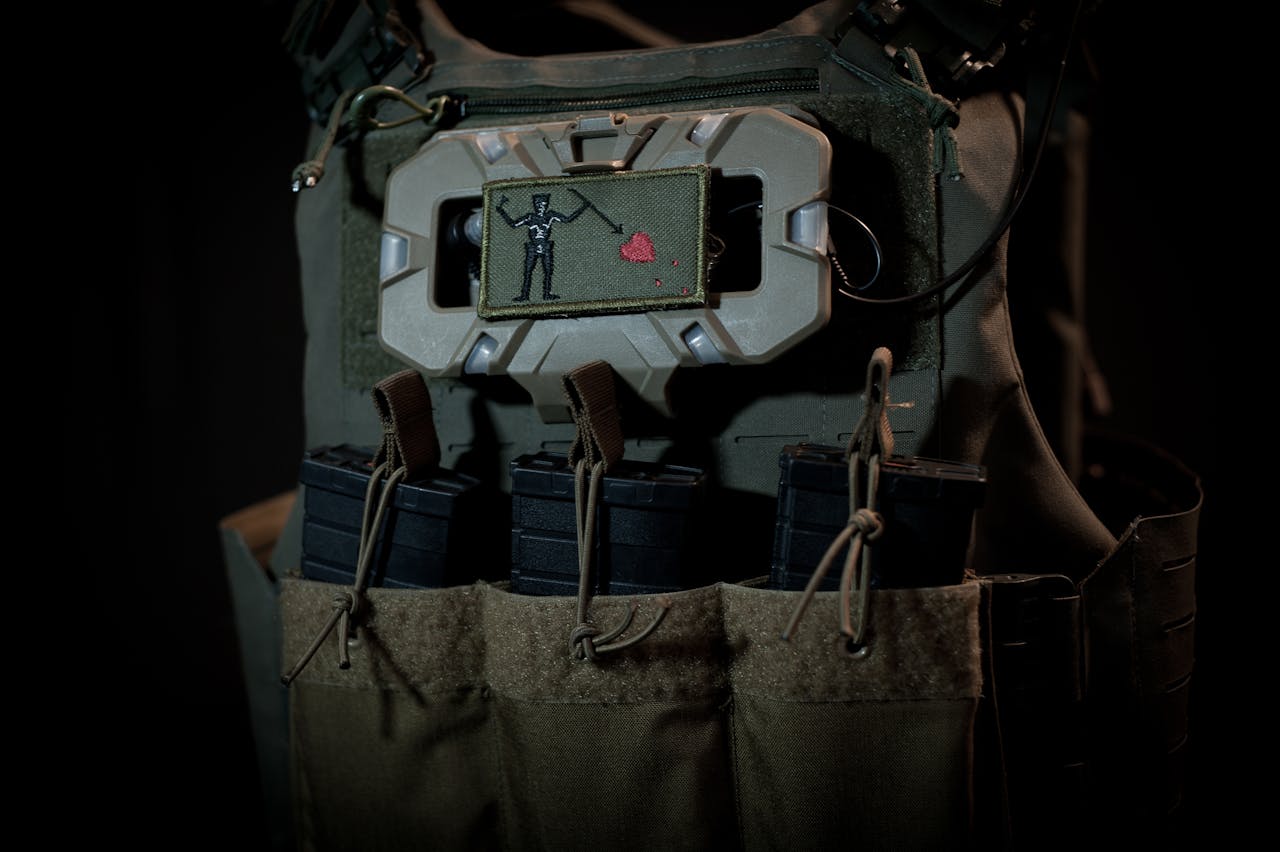 Close-up of a tactical vest with rifle magazines and a unique patch, dark background.