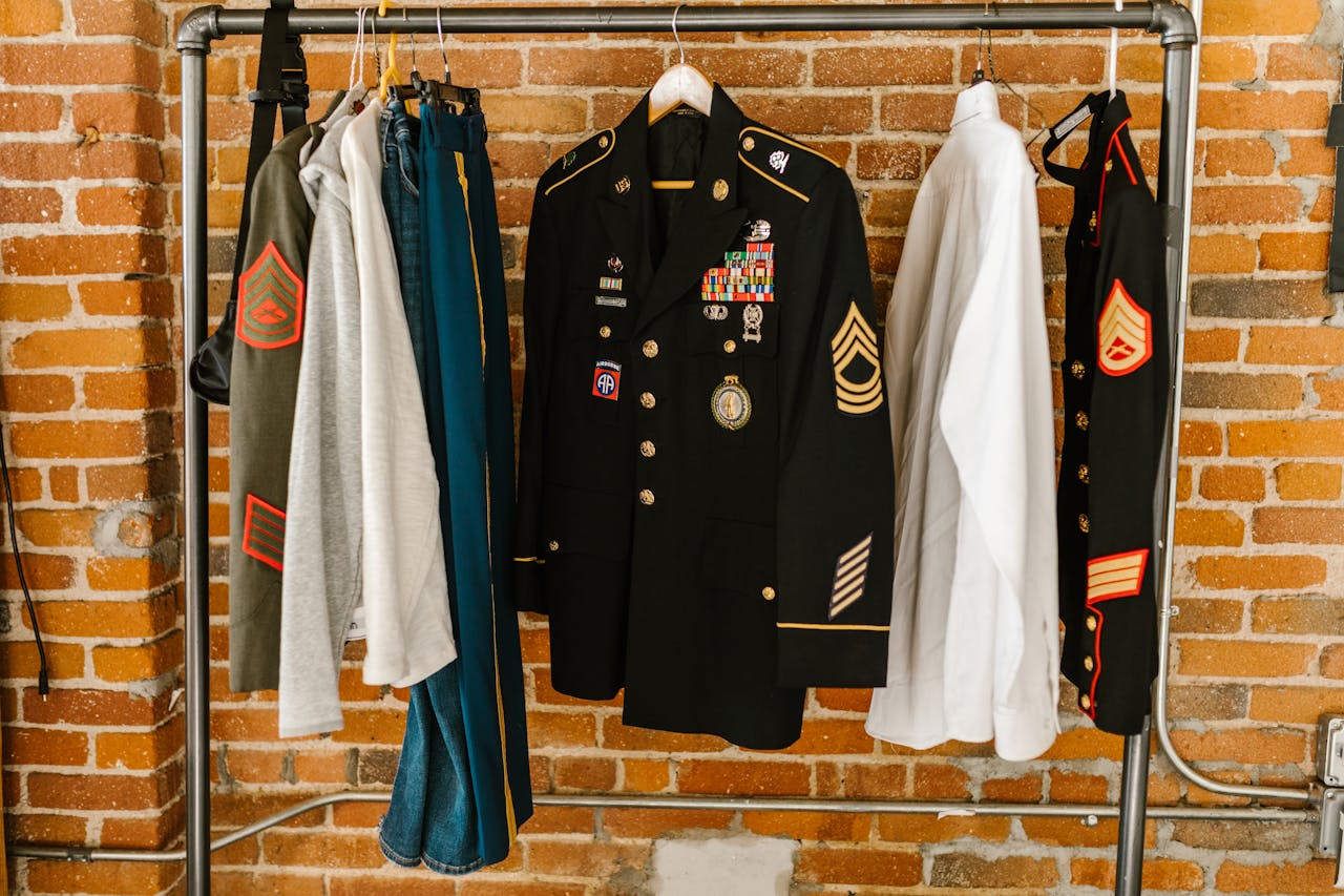 Military uniforms with badges hanging against a brick wall background.
